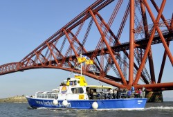 Tour boat painted blueand white alongside Forth Bridge